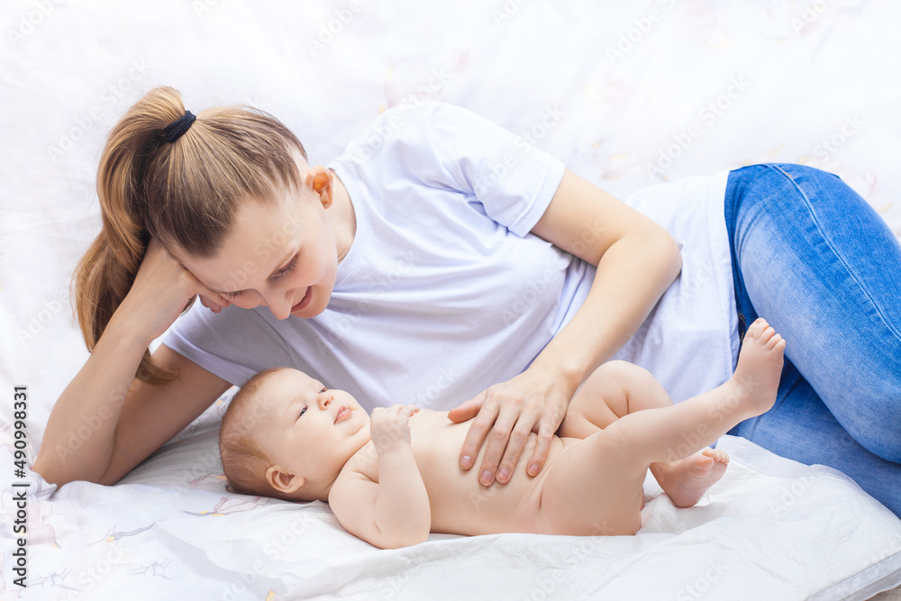young happy mother together with her newborn baby lie cheerfully on a white bed young happy mother together with her newborn baby lie cheerfully on a white bed