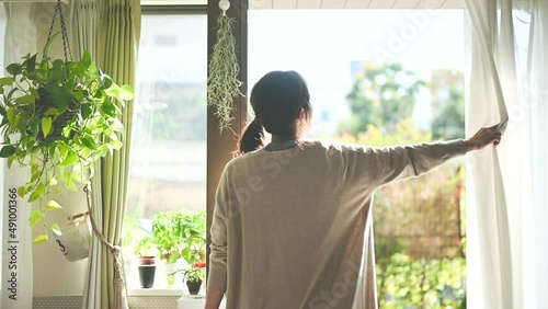 部屋のカーテンを開けて日光を浴びる女性