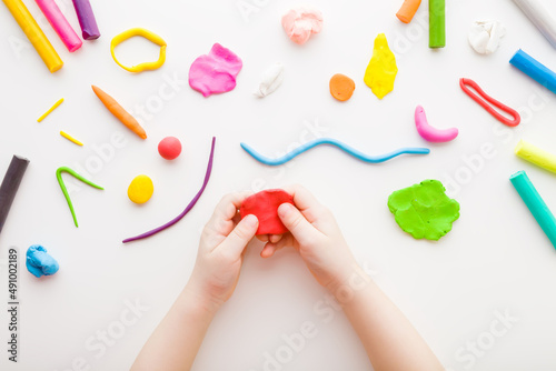 Foto Baby hands holding and kneading red modeling clay on white table background