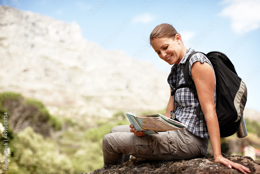 So many routes to be explored.... Young female hiker consulting her map while sitting on a mountain top.