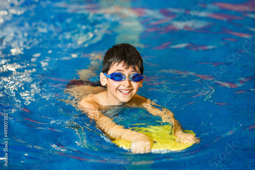 Canvas Print A little boy of 10 years learns to swim in the sport pool using a board