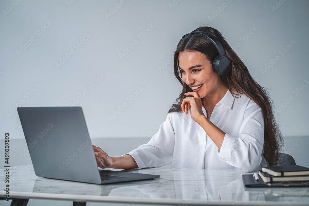 Businesswoman with laptop wearing headphones, office room Businesswoman with laptop wearing headphones, office room