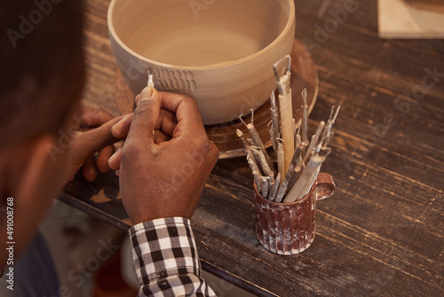 Experienced potter making designs on earthenware with ceramic tool photo