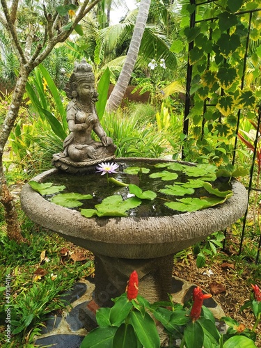 Beautiful outdoor garden setting with vintage stone statue overlooking a tropical water lily fountain