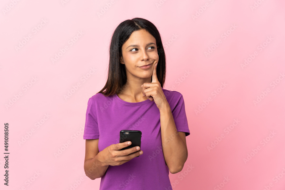 Caucasian girl isolated on pink background using mobile phone and thinking Caucasian girl isolated on pink background using mobile phone and thinking