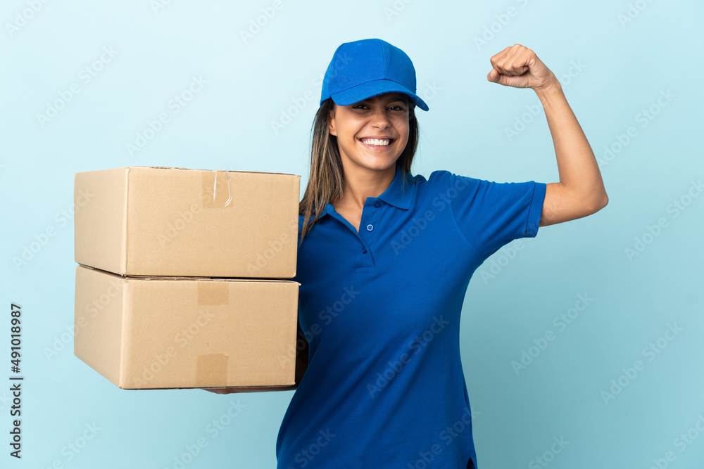 Young delivery woman isolated on blue background doing strong gesture Young delivery woman isolated on blue background doing strong gesture