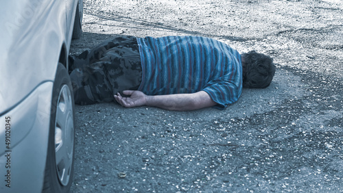the body of a dead man lies under a car on the road after a car crash