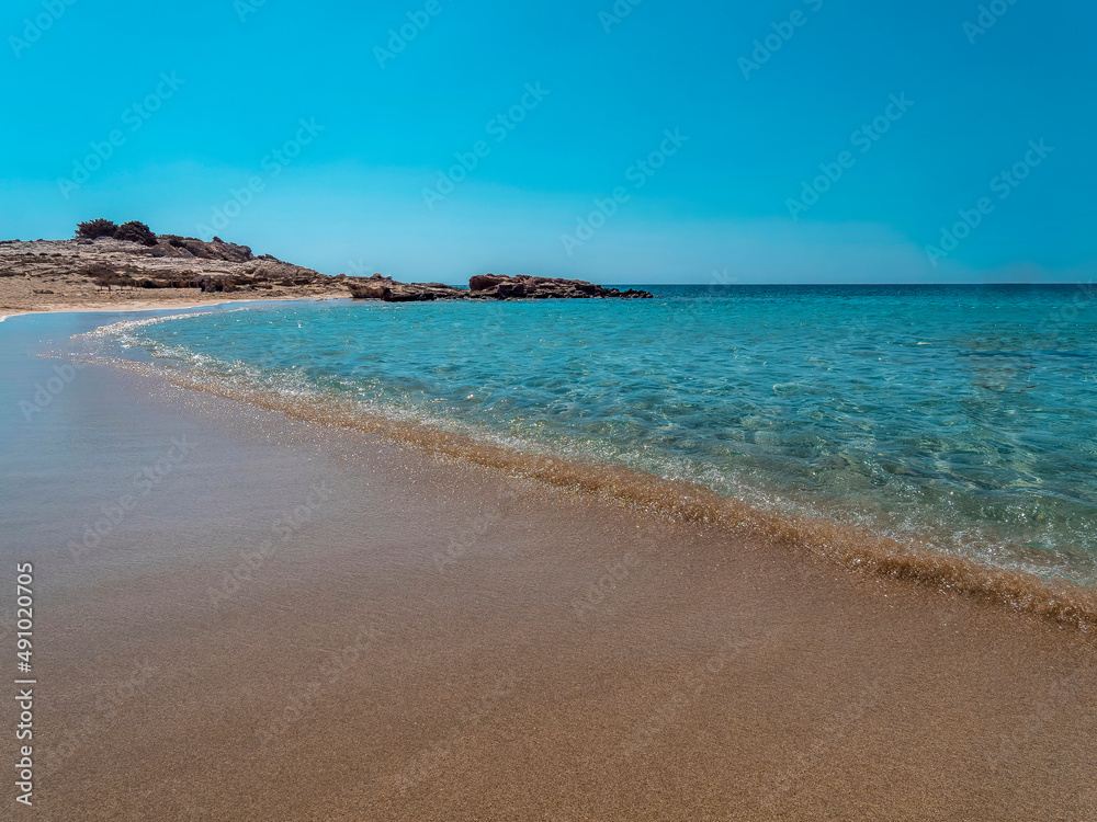 smooth waves of a turquoise sea gently touch the sandy Diakofti beach, Karpathos island, Greece.