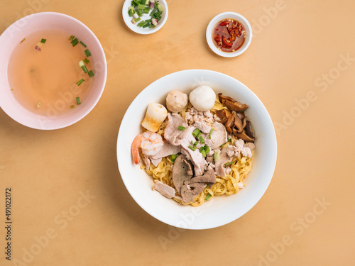 Black Soya Sauce Noodle in a bowl with soup, chili sauce and spring onion top view on wooden table