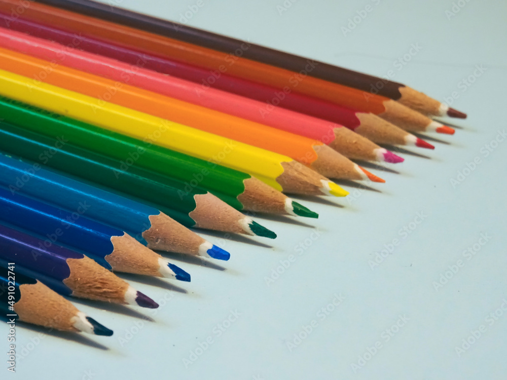 Diagonal view of a row of colored pencils over a blue background. Colour crayons. Selective Focus. Diagonal view of a row of colored pencils over a blue background. Colour crayons. Selective Focus.