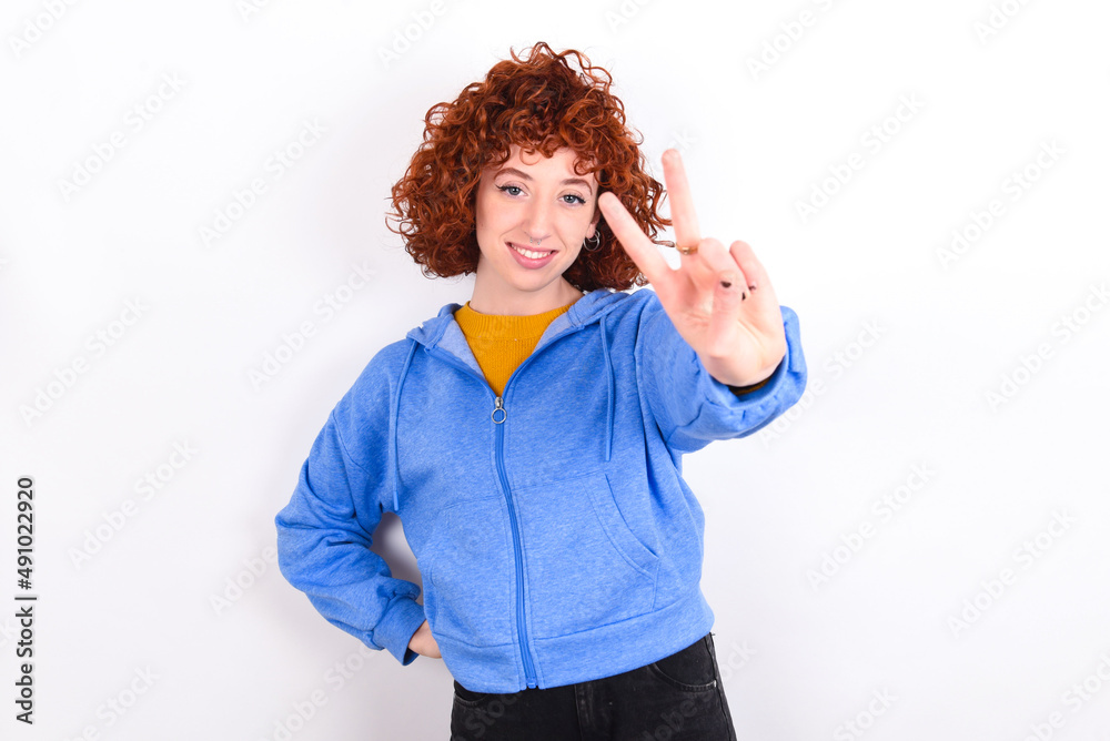 young redhead girl wearing blue jacket over white background directs fingers at camera selects someone. I recommend you. Best choice