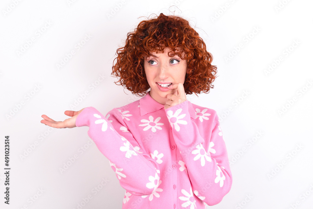 Positive young redhead girl wearing pink floral t-shirt over white background advert promo touches teeth with finger. Positive young redhead girl wearing pink floral t-shirt over white background advert promo touches teeth with finger.