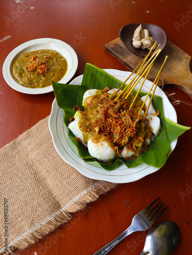 Sate Padang or satay padang is Spicy beef satay from Padang, West Sumatra. Served with spicy curry sauce and rice cake, lontong on banana leaf. isolated on white background
 photo