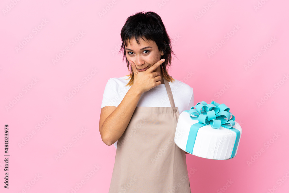 Uruguayan Pastry chef holding a big cake over isolated pink background thinking an idea Uruguayan Pastry chef holding a big cake over isolated pink background thinking an idea