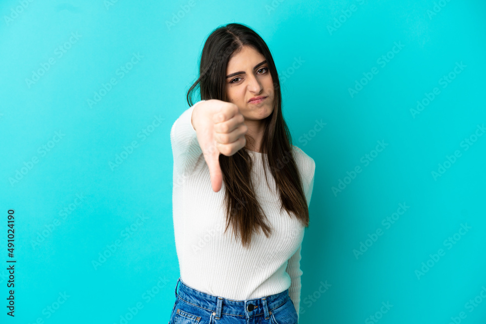 Young caucasian woman isolated on blue background showing thumb down with negative expression
