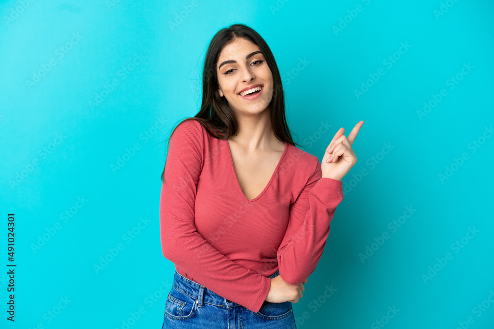 Young caucasian woman isolated on blue background happy and pointing up Young caucasian woman isolated on blue background happy and pointing up