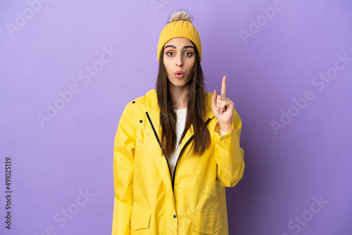 Young caucasian woman wearing a rainproof coat isolated on purple background intending to realizes the solution while lifting a finger up