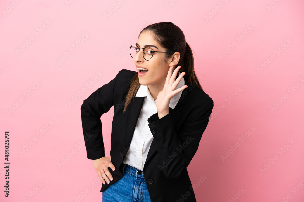 Young caucasian business woman isolated on pink background listening to something by putting hand on the ear Young caucasian business woman isolated on pink background listening to something by putting hand on the ear
