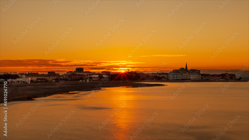 Alba, sole che sorge sopra la città dell'isola di grado vista dalla laguna del mare.