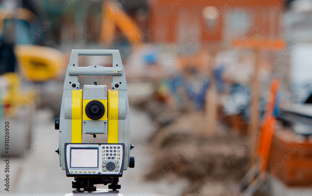 Yellow equipment set out on tripod on building site against cloudless blue sky. Construction site surveying engineering equipment, EDM, tacheometer set out on tripod site ready for setting out. Yellow equipment set out on tripod on building site against cloudless blue sky. Construction site surveying engineering equipment, EDM, tacheometer set out on tripod site ready for setting out.