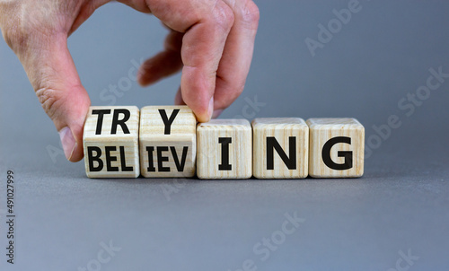 Trying and believing symbol. Businessman turns wooden cubes and changes the word Believing to Trying. Beautiful grey table grey background, copy space. Business, trying and believing concept.