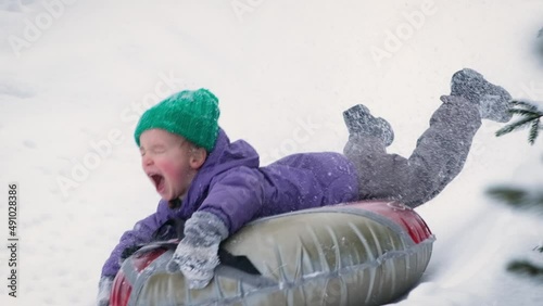 Snow tubing. Funny little child boy riding on inflatable tube. Kid sledding slide down hill. Winter fun activity outdoor.