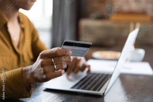 Female hand holding credit card at laptop close up. Young Black customer, shopaholic woman making payment for purchase on Internet, bank transactions, mortgage fees, buying on shop websites photo
