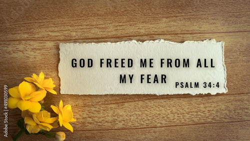 Top view of Bible verse God freed me from all my fear. Yellow flower and wooden background.