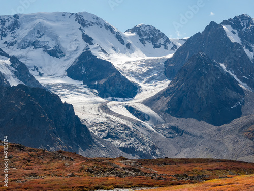 Scenic mountain landscape with big winding glacier on rocky hill. Awesome scenery with stony pass with snow in sunlight.