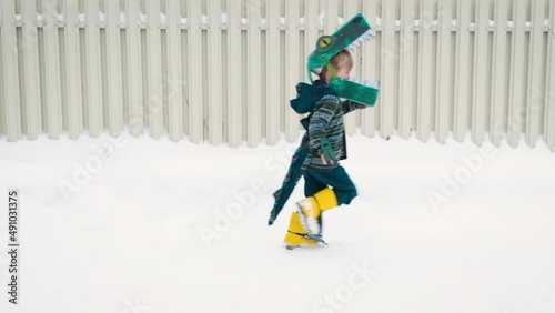 Funny playful little child boy in homemade cardboard textile dinosaur or crocodile costume running on snowy road.