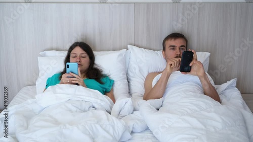 Couple man and woman lying in bed with smartphones, pay no heed to each outher. Digital detox. Technology internet addiction.  Dependence concept. photo