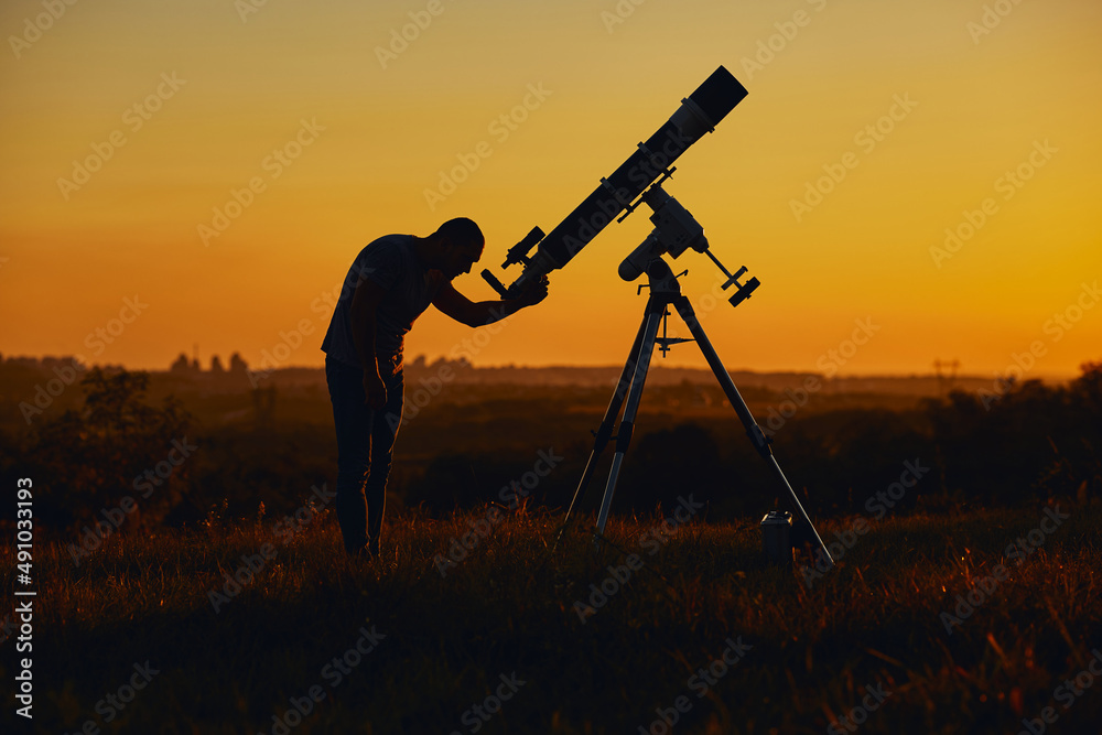 Silhouette of a man, astronomical telescope and countryside.