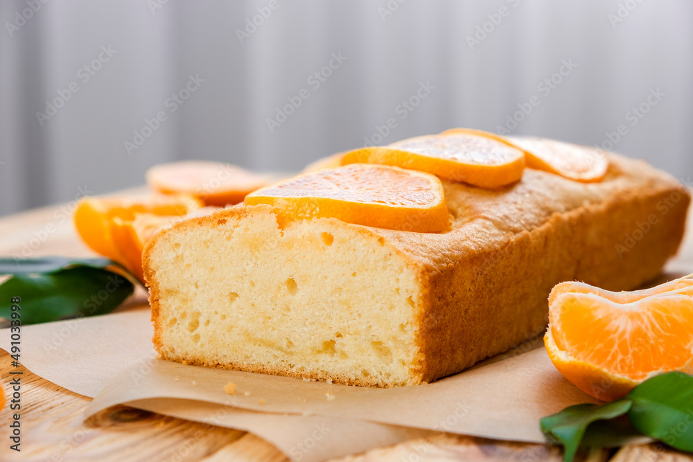 Loaf of gluten free tangerine cake with pieces of mandarin on rustic wooden background. Slice of citrus pie by classic recipe. Healthy nutrition, homemade vegan dessert.
