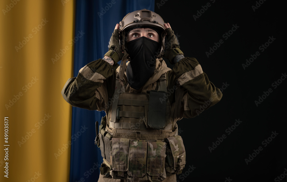 a male soldier in a military uniform and helmet on the background of the national flag of Ukraine