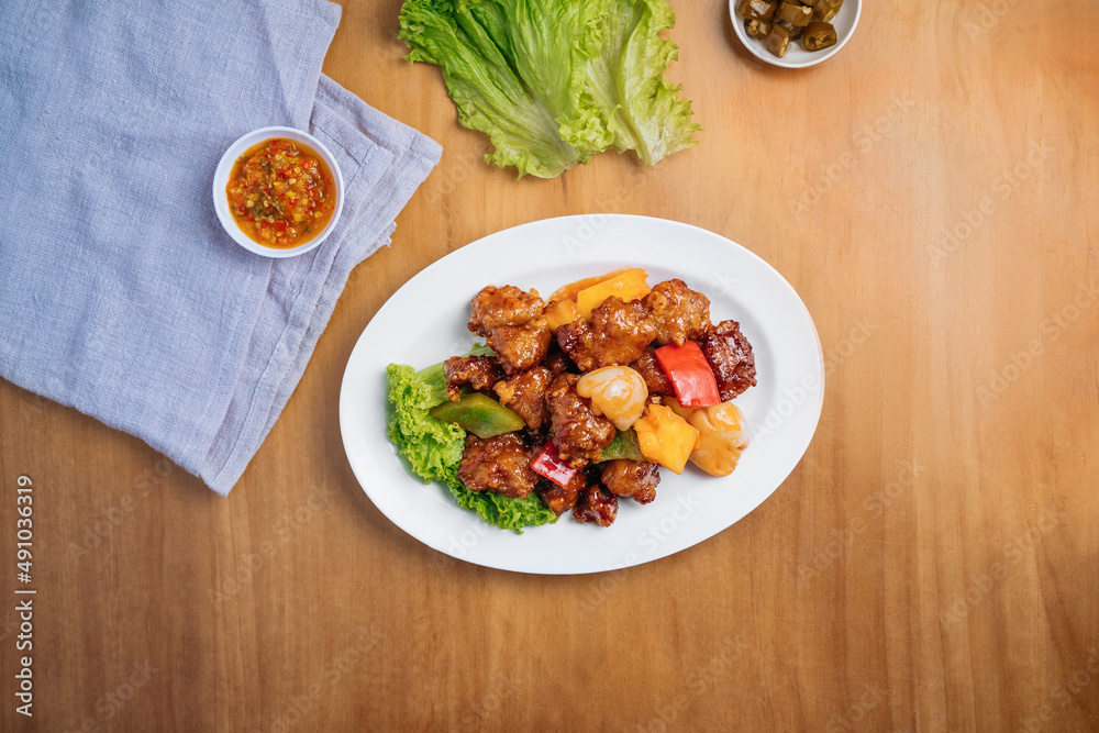 Chinese food Sweet and Sour Pork in a dish with chili sauce, and king's salad leaf top view on wooden background Chinese food Sweet and Sour Pork in a dish with chili sauce, and king's salad leaf top view on wooden background