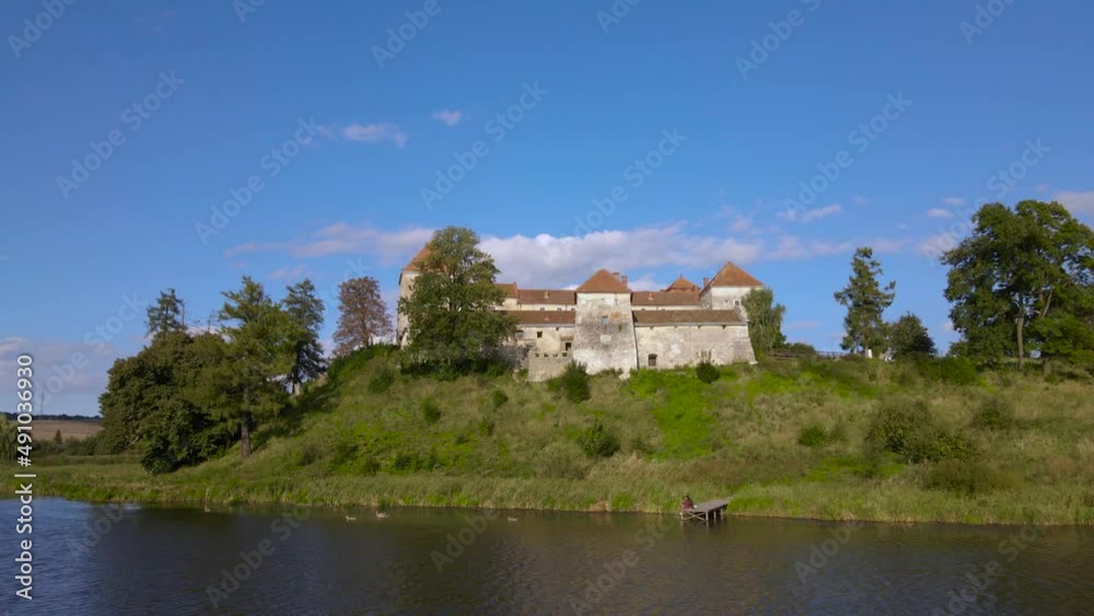 Aerial drone shot of historic castle on hill near lake, medieval architecture and cultural landmark in rural Svirzh, near Lviv Ukraine on warm sunny summer day. Tourist and travel attraction. Aerial drone shot of historic castle on hill near lake, medieval architecture and cultural landmark in rural Svirzh, near Lviv Ukraine on warm sunny summer day. Tourist and travel attraction.