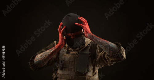 photo of a man in a military uniform and balaclava with a bloody face and hands up to the elbow in blood on a black background