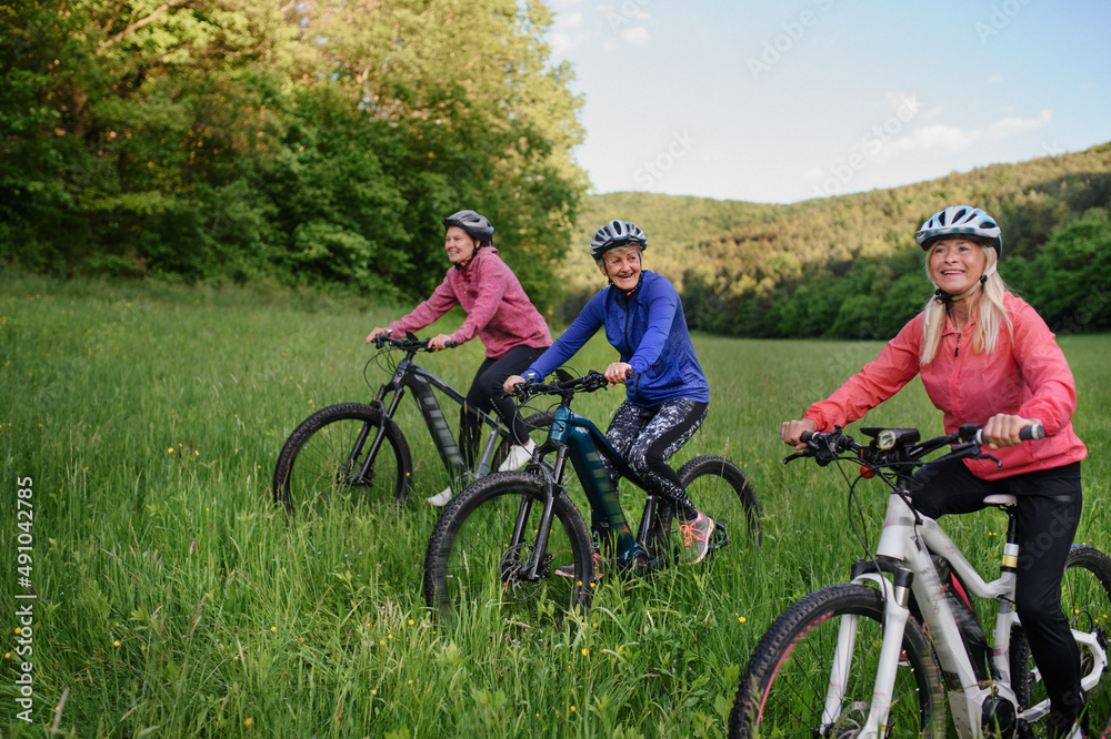 Happy active senior women friends cycling together outdoors in nature.