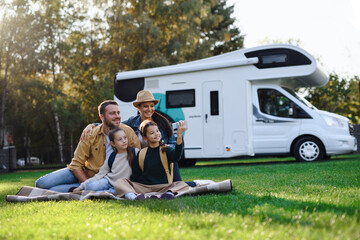 Happy young family with two children ltaking selfie with caravan at background outdoors.