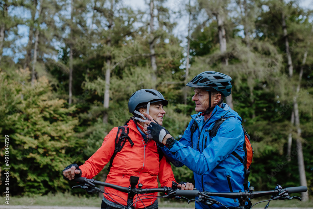 Senior couple bikers putting on cycling helmet outdoors in forest in autumn day. Senior couple bikers putting on cycling helmet outdoors in forest in autumn day.