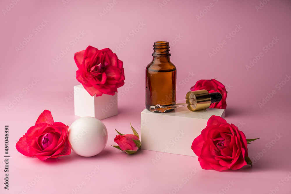Glass bottle for drops and liquid and oils. Advertising of a cosmetology product. Roses. Pink water. OilFor Face and Body Glass bottle for drops and liquid and oils. Advertising of a cosmetology product. Roses. Pink water. OilFor Face and Body