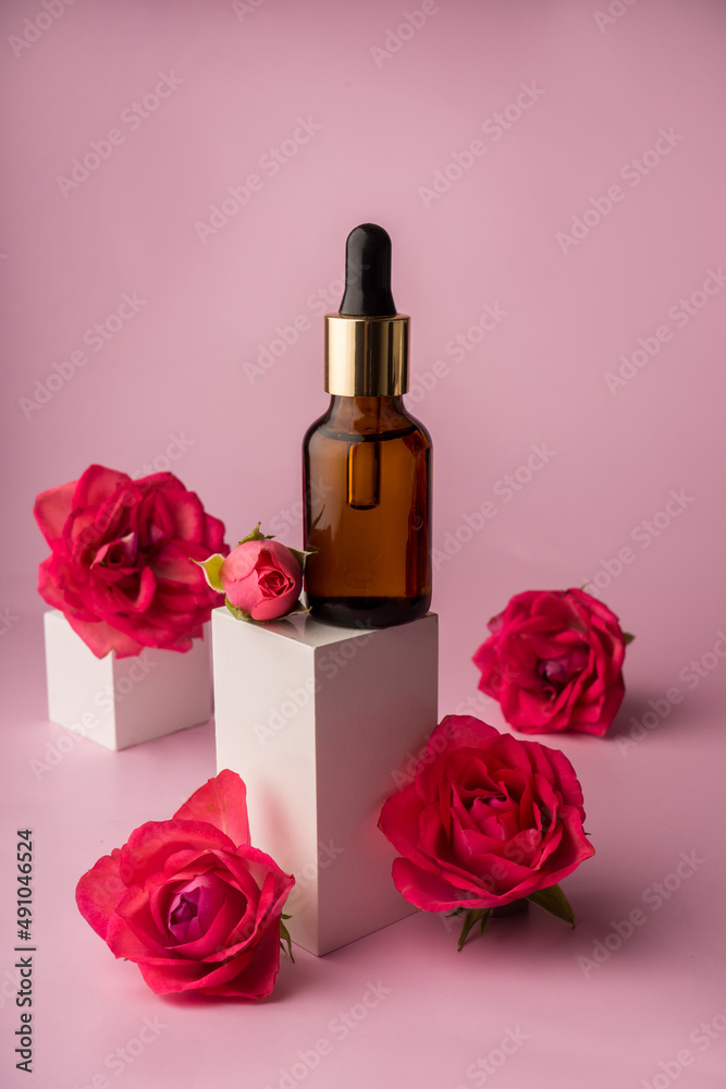 Glass bottle for drops and liquid and oils. Advertising of a cosmetology product. Roses. Pink water. OilFor Face and Body Glass bottle for drops and liquid and oils. Advertising of a cosmetology product. Roses. Pink water. OilFor Face and Body