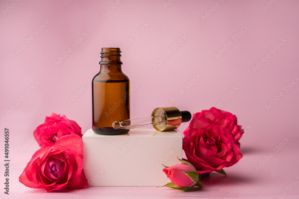 Glass bottle for drops and liquid and oils. Advertising of a cosmetology product. Roses. Pink water. OilFor Face and Body Glass bottle for drops and liquid and oils. Advertising of a cosmetology product. Roses. Pink water. OilFor Face and Body