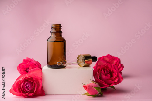 Glass bottle for drops and liquid and oils. Advertising of a cosmetology product. Roses. Pink water. OilFor Face and Body 
