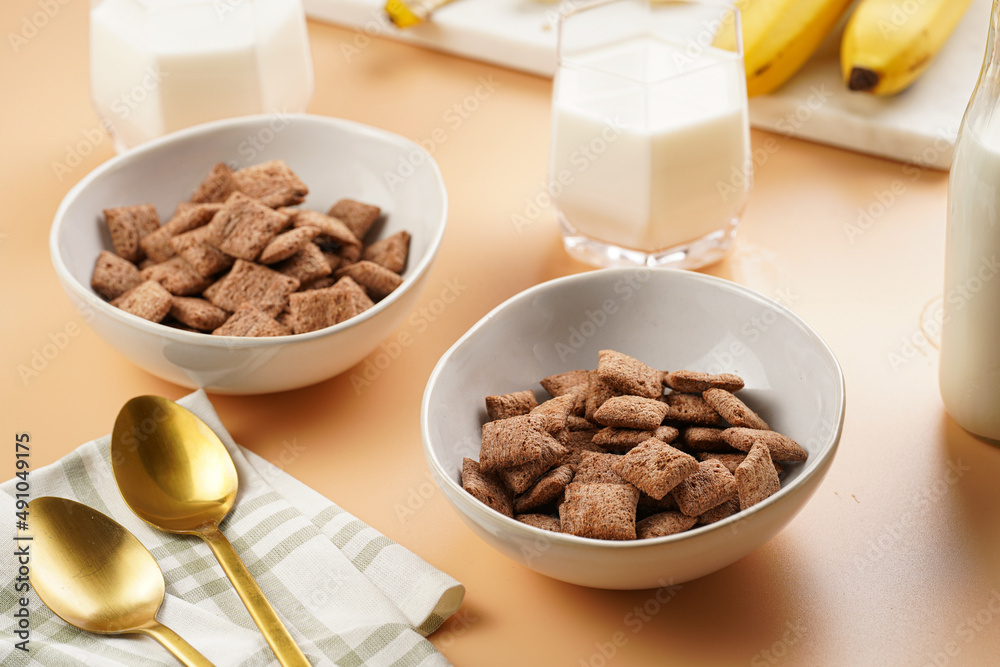 Nougat bites - sweet cocoa and hazelnut wheat puffed pillows - breakfast cereal in white bowls, glasses with milk on sunny orange background Nougat bites - sweet cocoa and hazelnut wheat puffed pillows - breakfast cereal in white bowls, glasses with milk on sunny orange background