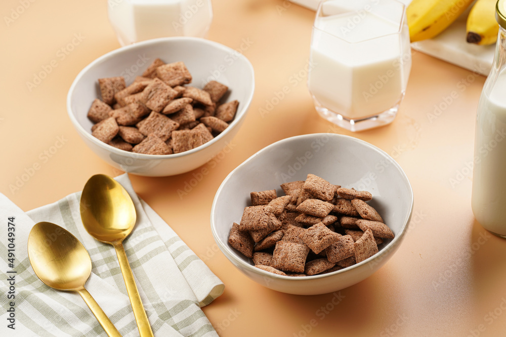 Nougat bites - sweet cocoa and hazelnut wheat puffed pillows - breakfast cereal in white bowls, glasses with milk on sunny orange background Nougat bites - sweet cocoa and hazelnut wheat puffed pillows - breakfast cereal in white bowls, glasses with milk on sunny orange background