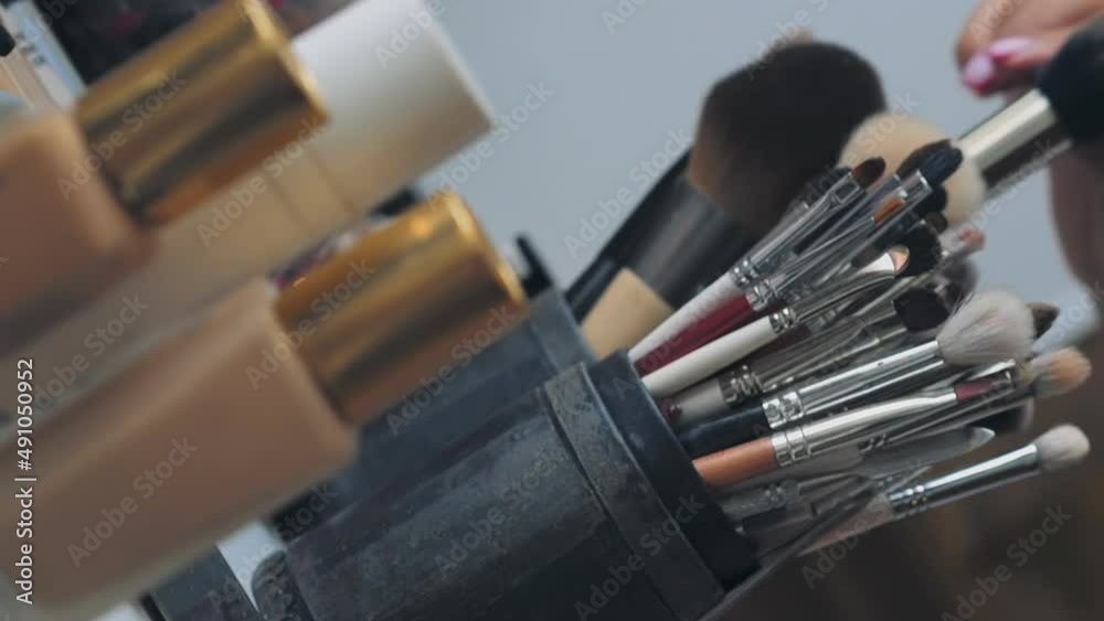 Makeup artist takes fluffy brush to work with client at table in contemporary beauty salon extreme closeup. Different tools and decorative cosmetics Makeup artist takes fluffy brush to work with client at table in contemporary beauty salon extreme closeup. Different tools and decorative cosmetics