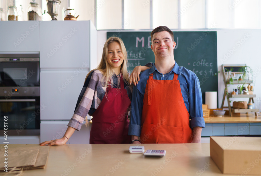 Young Down Syndrome waiter working with colleague in take away restaurant, social inclusion concept. Young Down Syndrome waiter working with colleague in take away restaurant, social inclusion concept.
