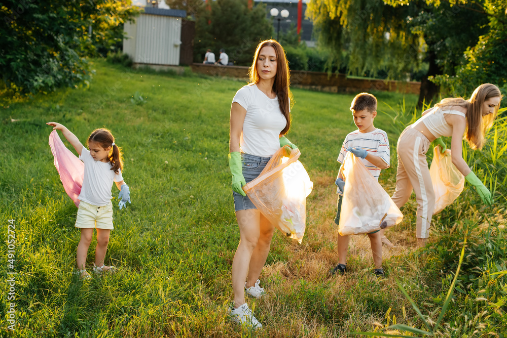 Fototapeta premium A group of adults and children together at sunset is engaged in garbage collection in the park. Environmental care, waste recycling. Sorting garbage.