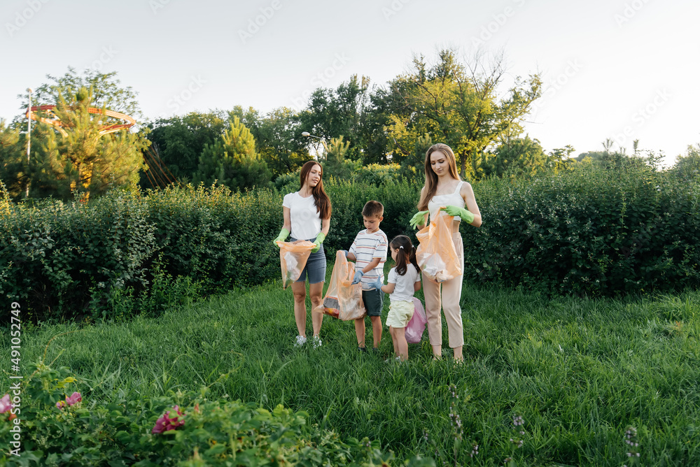 Obraz premium A group of adults and children together at sunset is engaged in garbage collection in the park. Environmental care, waste recycling. Sorting garbage.